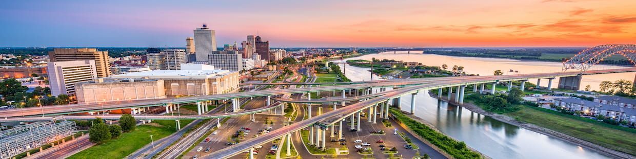 Aerial view of a vibrant Arizona city skyline at sunset, with a river on the right. Bridges and highways crisscross through the city, which offers stunning scenery for those pursuing Online Education Programs. Buildings glow warmly, with green spaces and parking lots near the water.